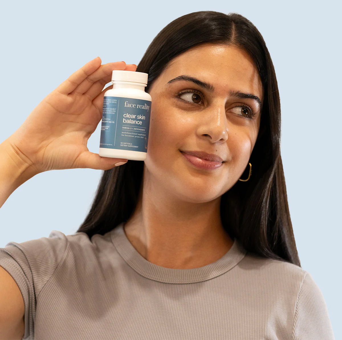 Woman holding a bottle of 'face realty' clear skin balance product against a light blue background