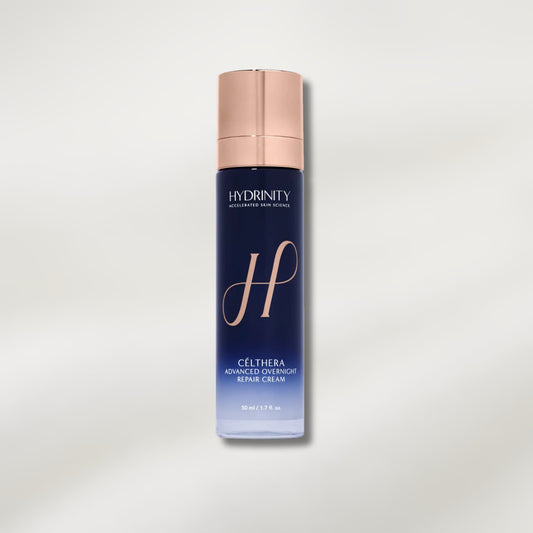 Hydrinity Gélthera Advanced Overnight Repair Cream in a tall, dark blue cylindrical bottle with a metallic rose gold cap, set against a clean, light gray gradient background.