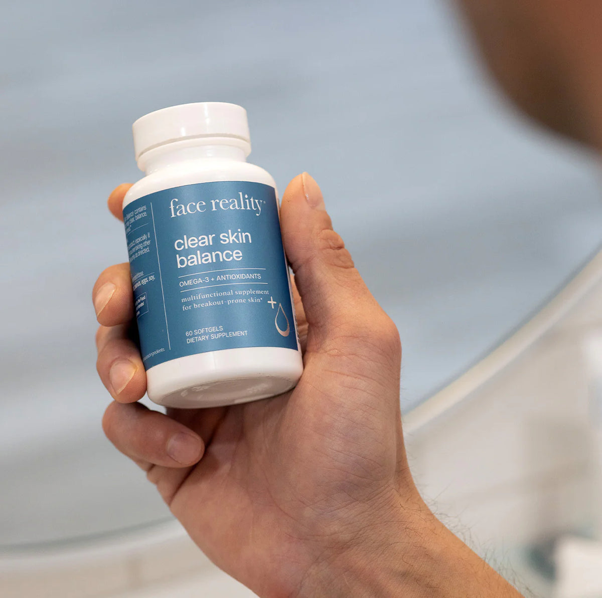 Hand holding a bottle labeled 'face reality clear skin balance' against a neutral background