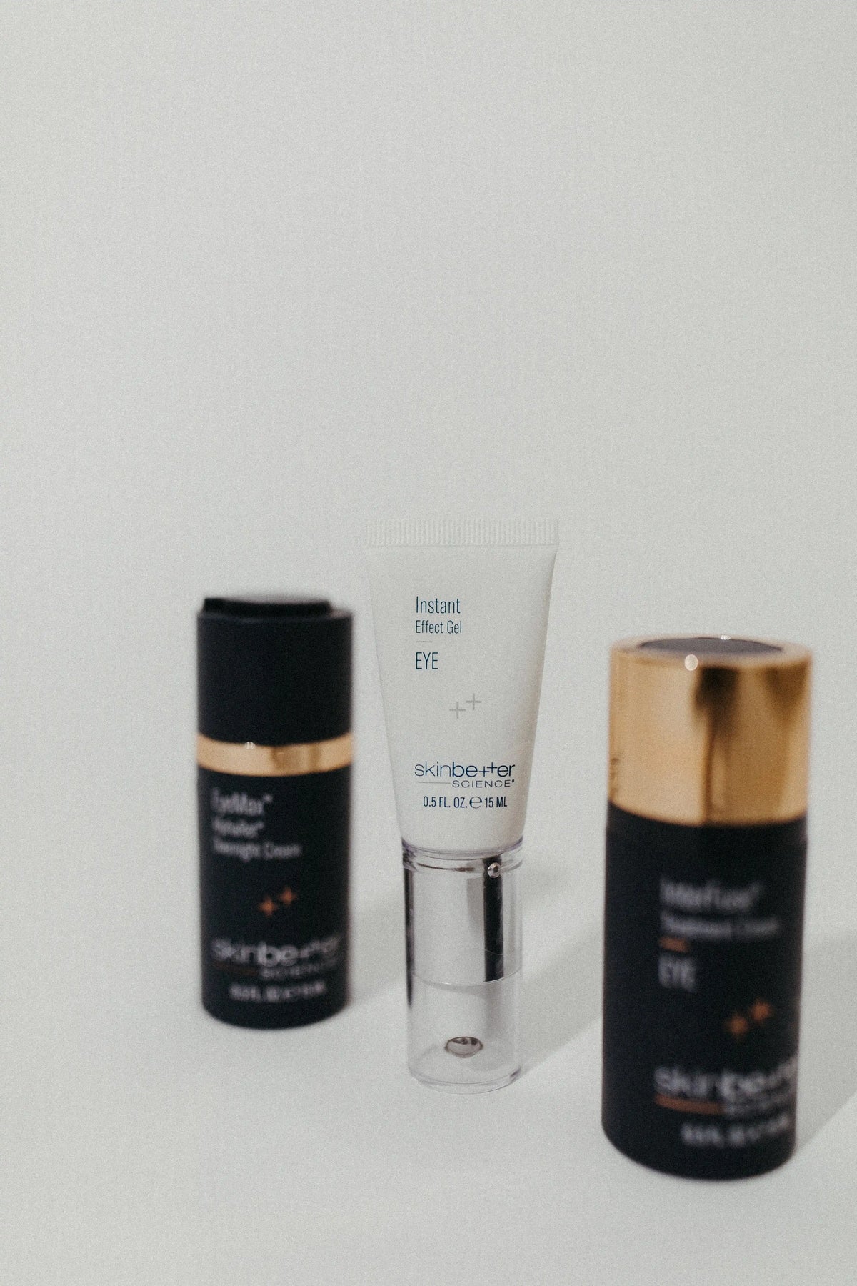 Three skincare products from the brand surbeauty arranged on a light gray surface against a white background: a black tube with a gold band on the left, a white squeeze tube with a clear cap in the center, and a black tube with a gold cap on the right.